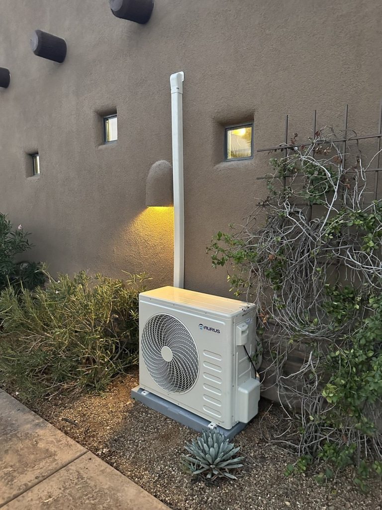 Outdoor mini split condenser unit mounted beside a home's exterior wall